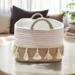 Hand-braided natural cotton rope shelf basket with decorative tassels, filled with folded blankets and plants, styled on a rustic wooden shelf for boho-chic home organization