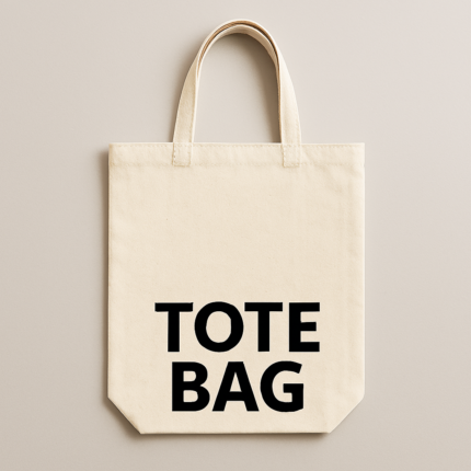 Image of a natural canvas tote bag laid flat on a light wood surface, accented with a green leaf sprig and wooden beads.